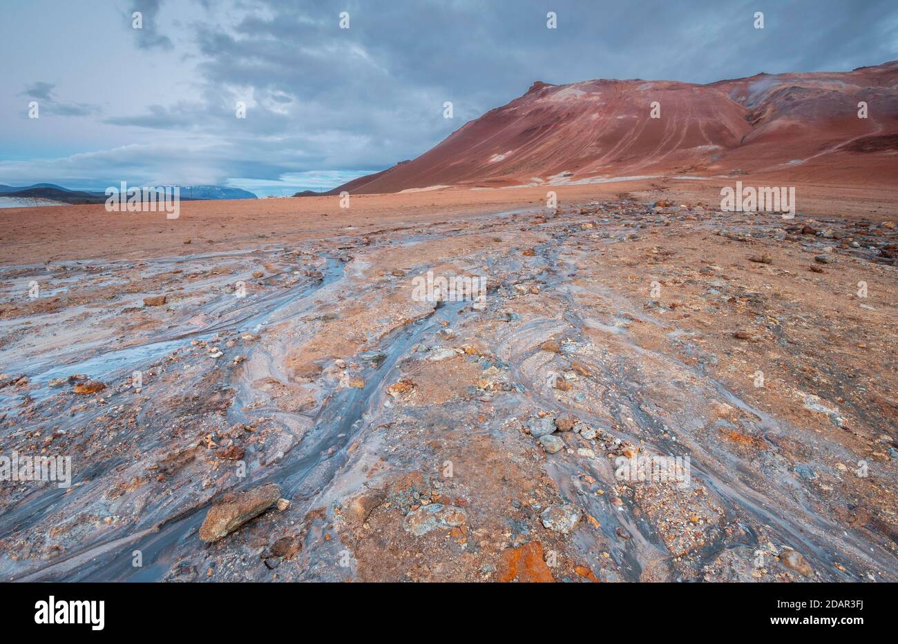 L'eau d'une source chaude coule au-dessus de la plaine rouge, dans la montagne d'arrière-plan Namafjall dans la zone haute température Hverir Hveraroend géothermique Banque D'Images