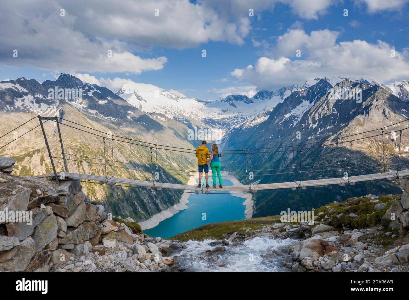 Randonneur, jeune femme et jeune homme sur un pont suspendu à l'Olpererhuette, vue sur le réservoir Schlegeis, réservoir Schlegeis, derrière le Banque D'Images