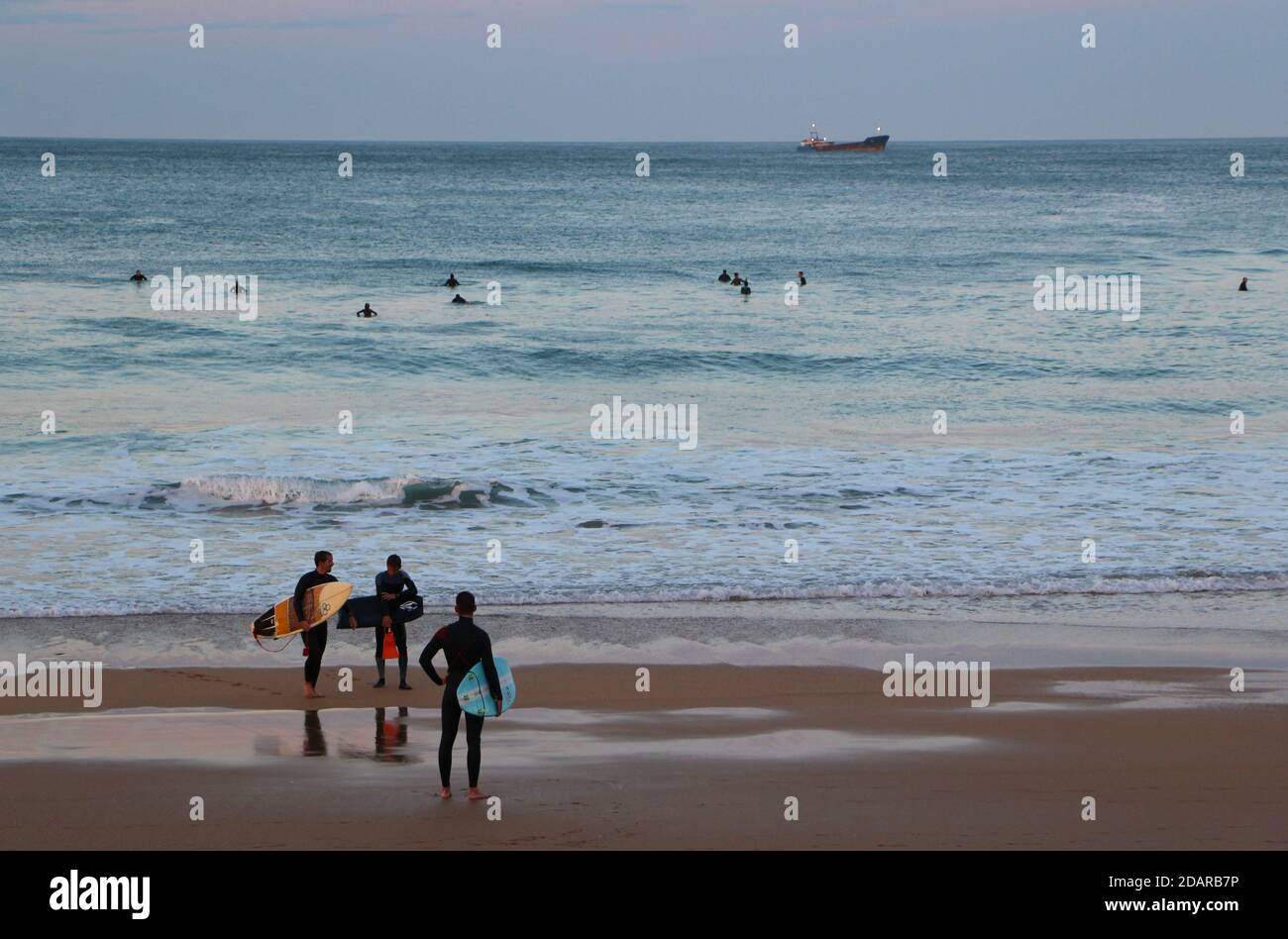 Trois surfeurs prêts à aller surfer sur la plage à Sardinero au crépuscule sur un doux soir d'automne Santander Cantabria Espagne a ancré navire Banque D'Images