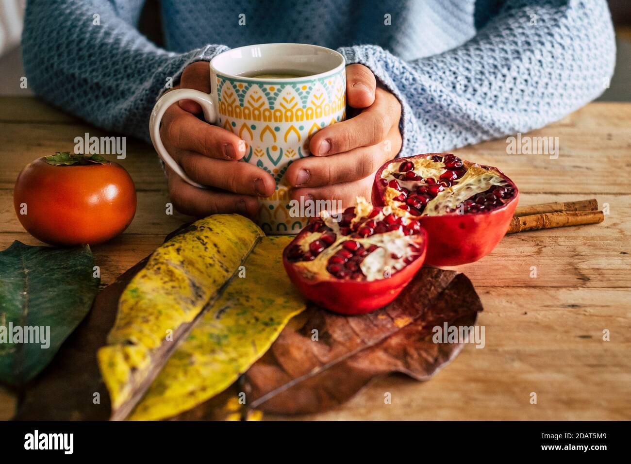 Gros plan de la scène automnale en intérieur avec paire de les mains tiennent une tasse de thé sur un jaune de bois et table orange avec pamplemousse et feuille Banque D'Images