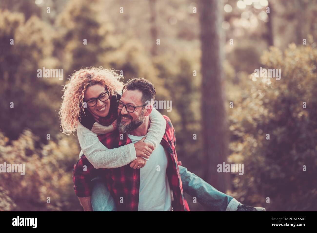 Couple adulte heureux profiter de la forêt de bois de la nature ensemble et à l'extérieur activité de loisirs avec plaisir et joie - homme porte femme sur son dos et les deux rigolent un l Banque D'Images