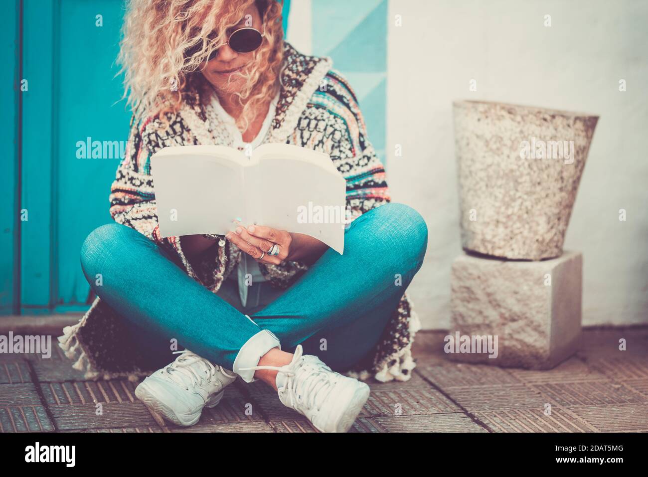 Magnifique portrait de femme assis sur le sol à l'extérieur lire un livre papier ou étudier à l'extérieur de la maison - jeune les adultes lisent et apprennent à profiter du Banque D'Images