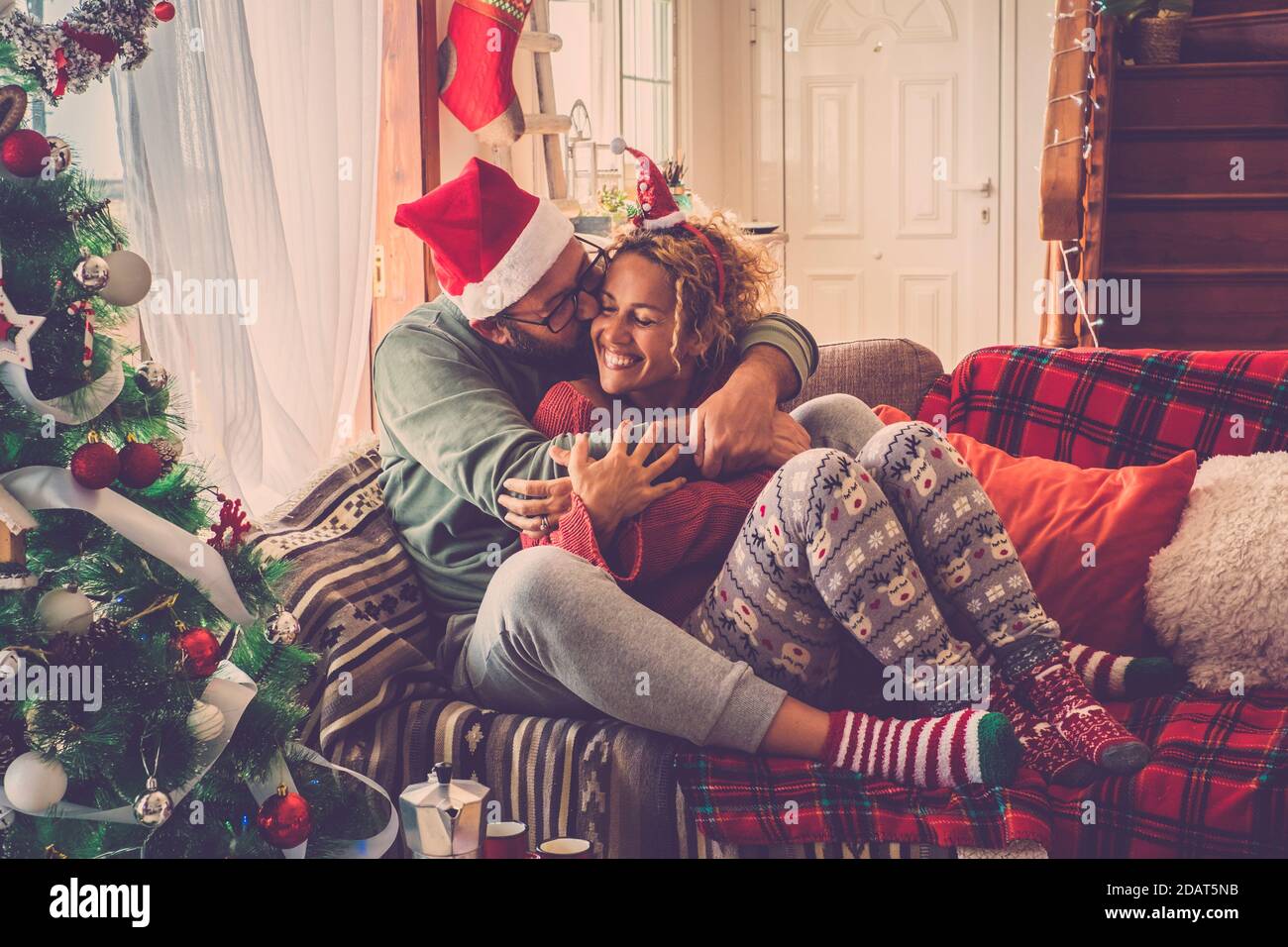 Couple amoureux appréciez et célébrez la veille de noël matin à maison embrassant et embrassant s'asseoir sur un coloré et canapé décoré à la maison - vin de vacances Banque D'Images
