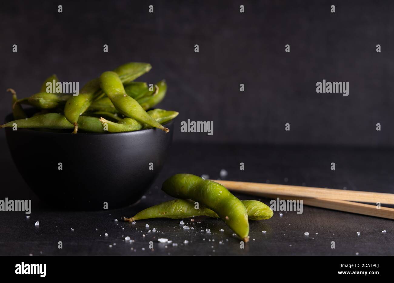Hors-d'œuvre japonaise haricots de soja vert Edamame assaisonnés avec du sel dans un bol, avec des bâtons de magasin sur le côté. Banque D'Images