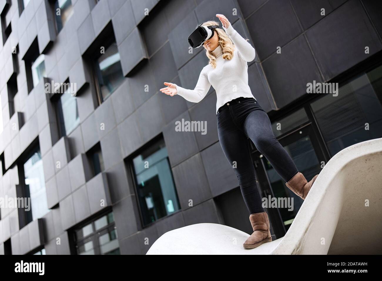 Jeune femme portant des lunettes de réalité virtuelle contre un bâtiment futuriste Banque D'Images