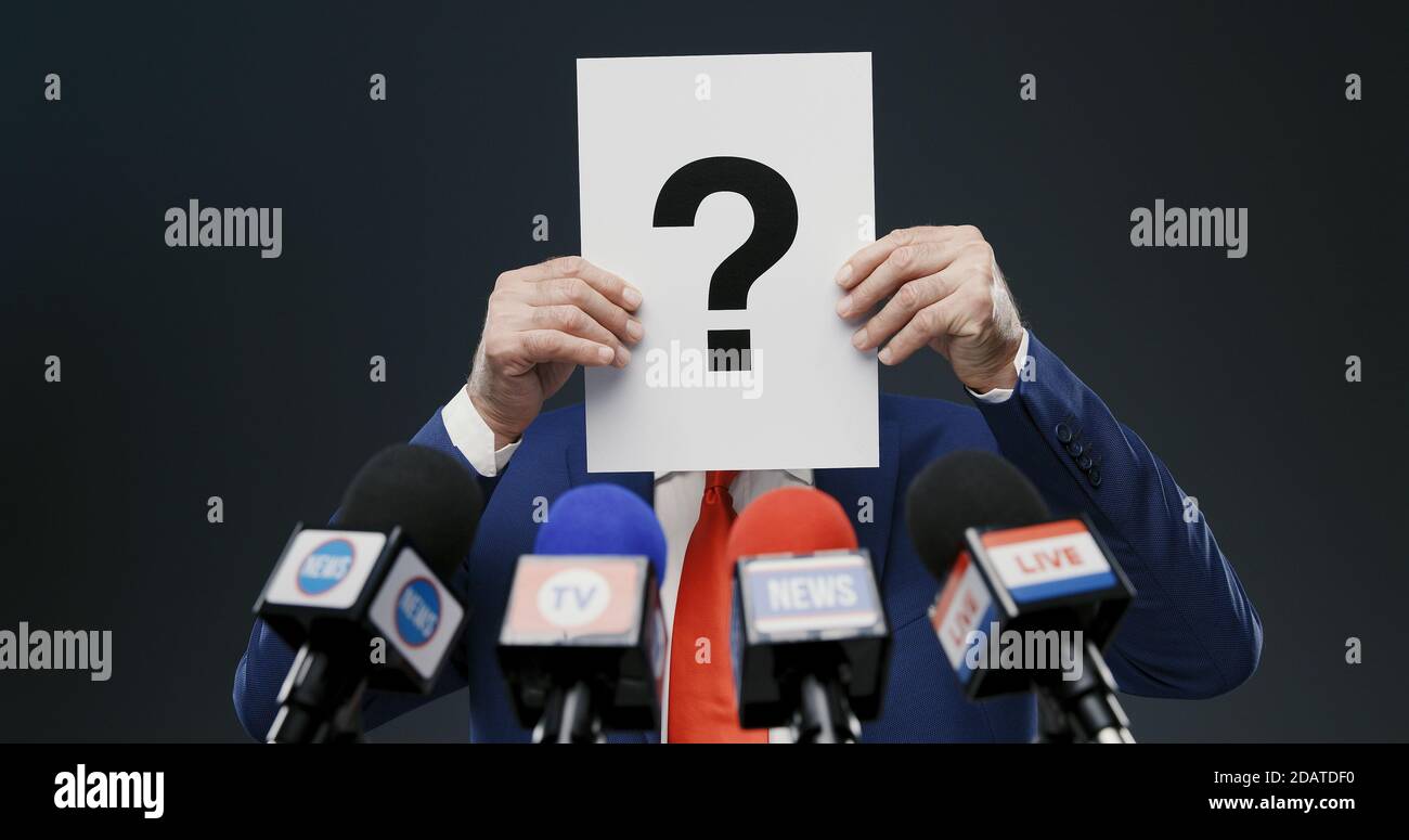 Homme politique cachant son visage avec un signe avec un point d'interrogation lors d'un entretien de presse, il cache son identité Banque D'Images