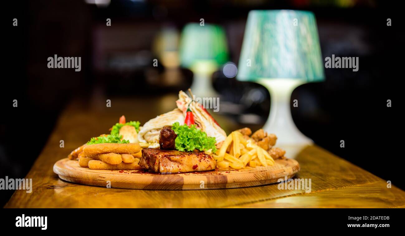 Menu snack-bar. Calories élevé pour le groupe d'amis. De délicieux en-cas savoureux. Snack pour la bière. Les repas au restaurant. Planche de bois avec beaucoup de frites et bâtonnets de poisson viande burrito steak servi avec une salade. Banque D'Images