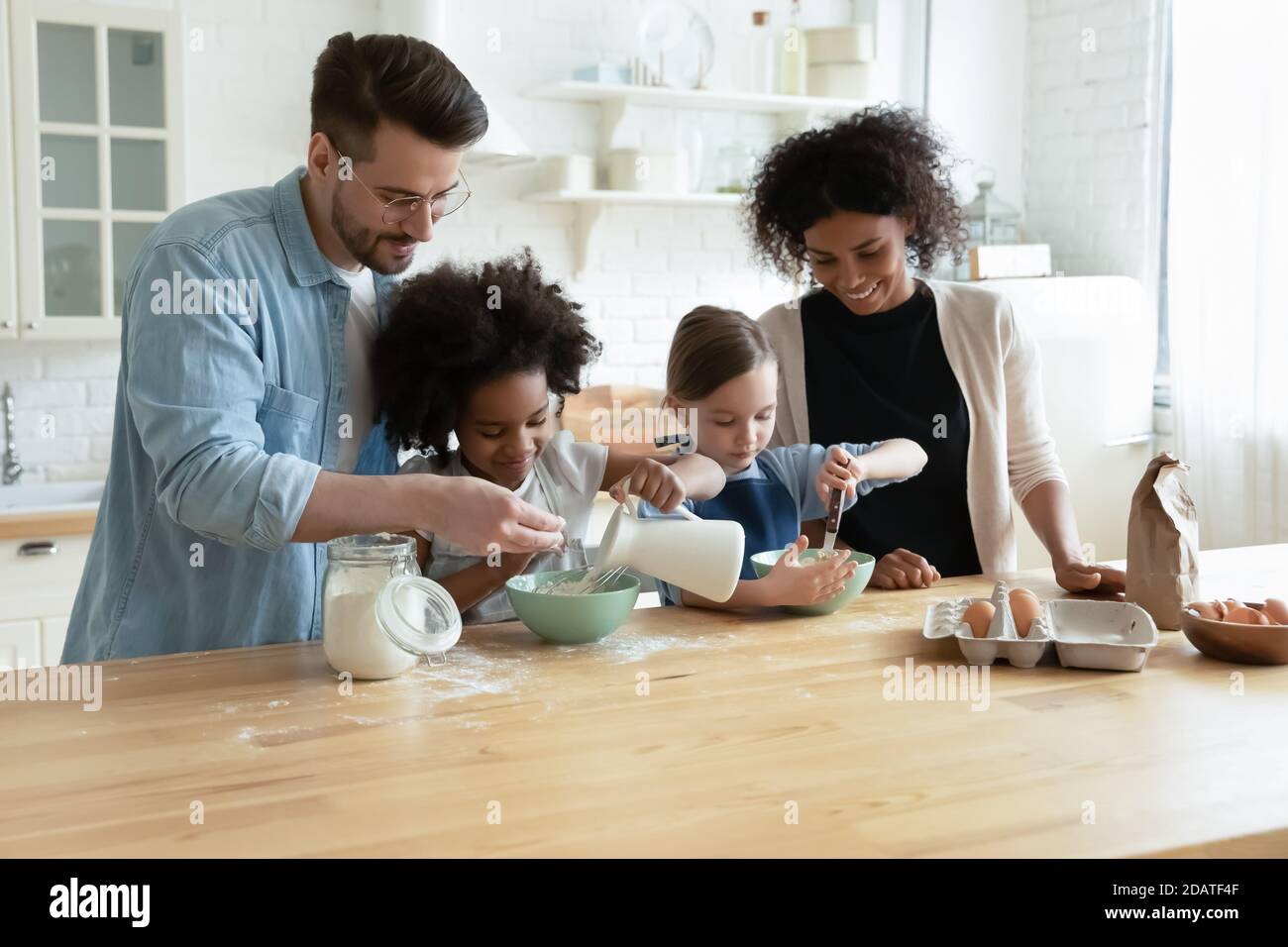 Joyeux parents divers avec des enfants cuisant de la pâte dans la cuisine moderne Banque D'Images