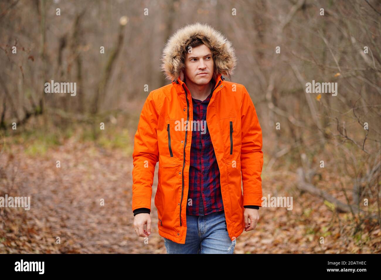 Jeune homme en cagoule et veste orange marchant dans la forêt d'automne.  Homme adulte à l'air frais en automne Photo Stock - Alamy