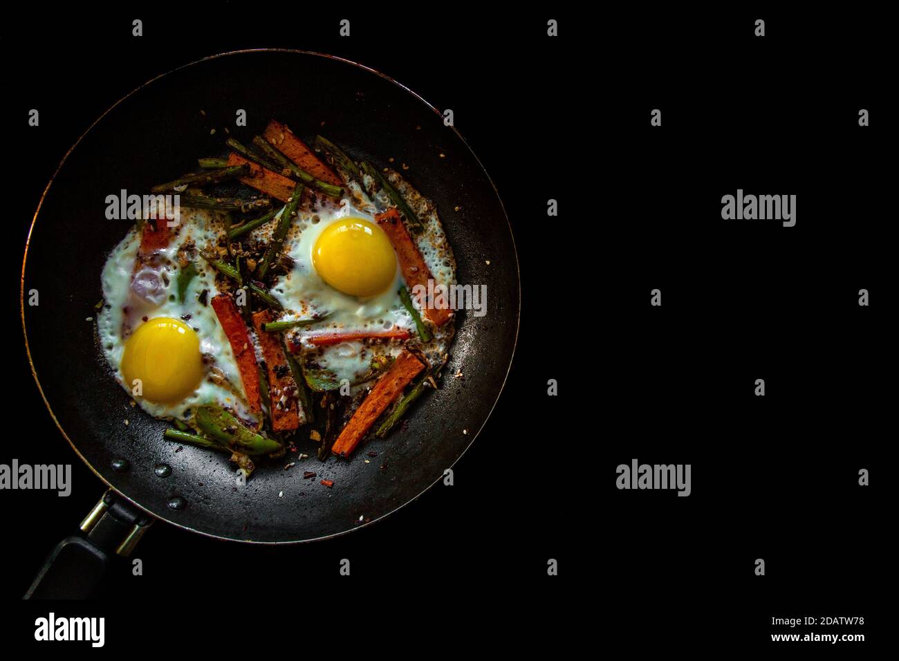 Deux œufs frits dans une casserole avec de grandes tranches de carottes, de poivron et d'asperges avec des épices et de la sauce. Banque D'Images