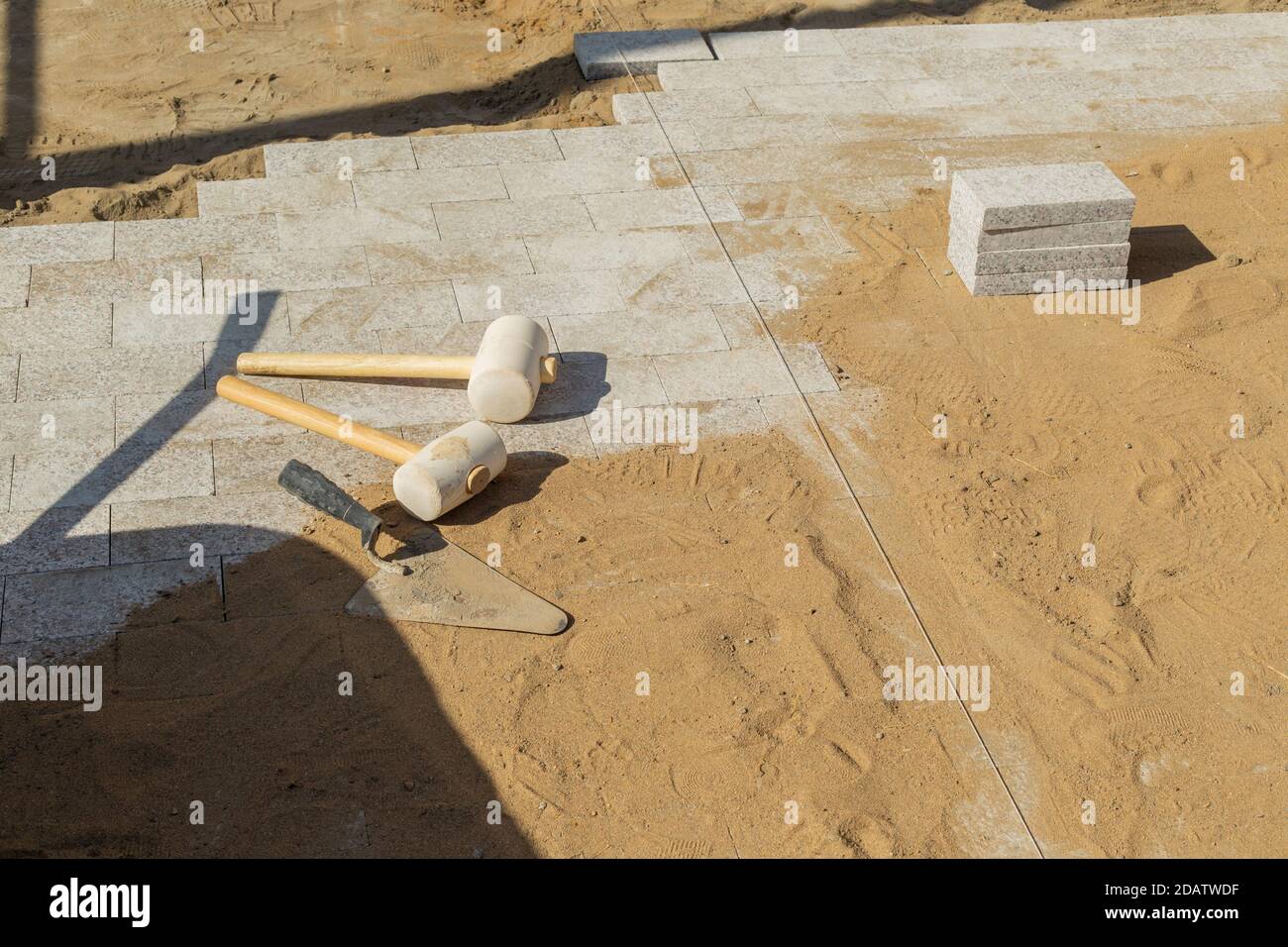 La truelle se trouve à côté de deux marteaux en caoutchouc pour poser des carreaux de sol sur des lingots de granit. Banque D'Images