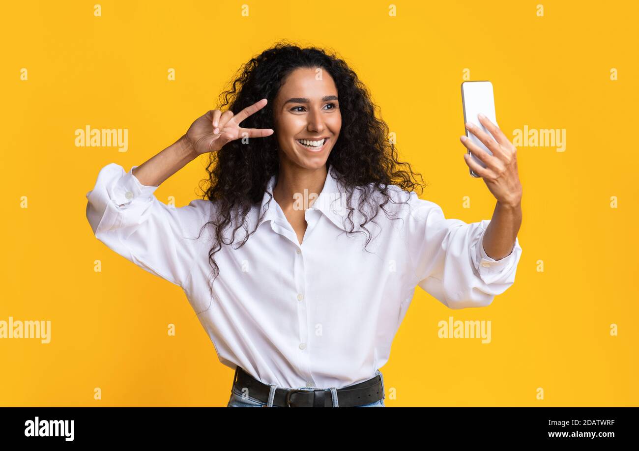 Positive Millenium Lady prend Selfie sur smartphone et montre la paix Geste Banque D'Images