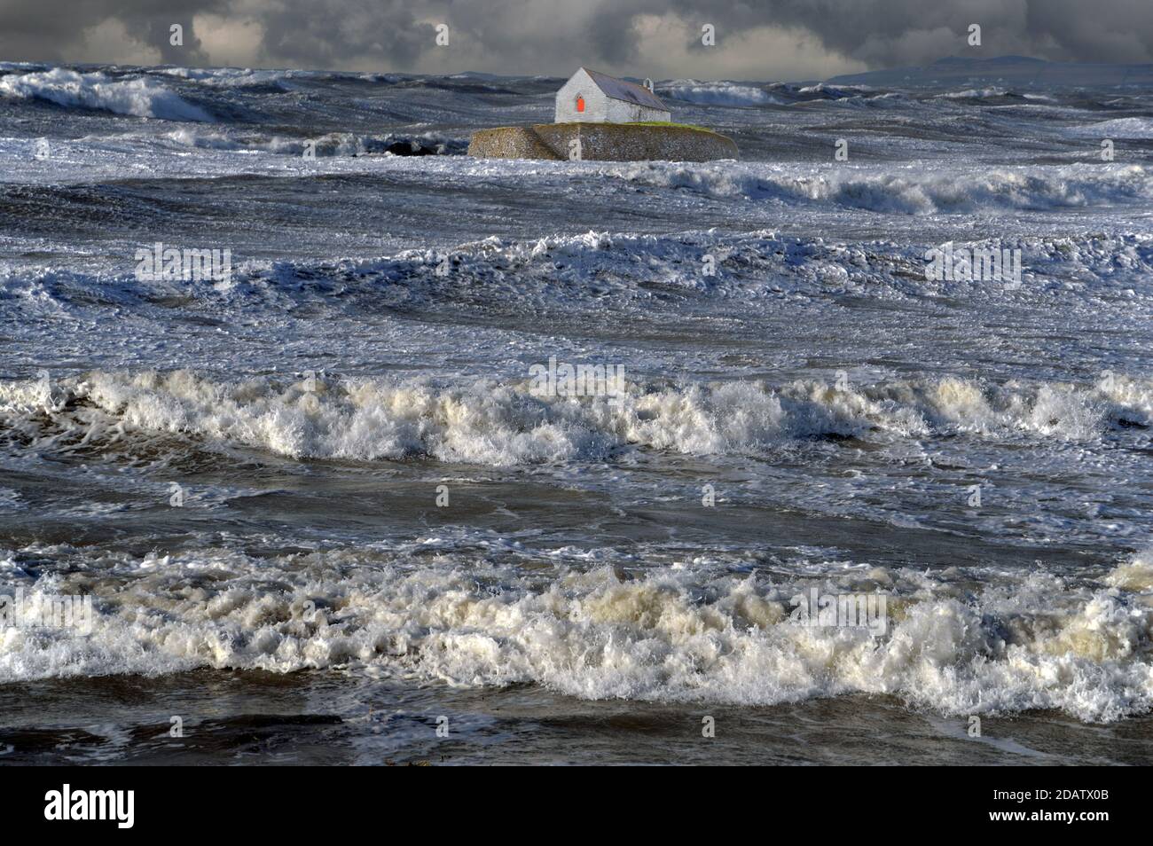 St Cwyfan's est une église datant de 12 ans située sur l'île marécageuse de Cribinau, Anglesey. Dans cette image de fantaisie, la mer rugueuse a été ajoutée. Banque D'Images