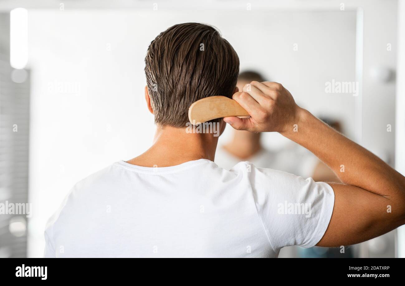 Jeune homme regardant dans le miroir se brossant les cheveux Banque D'Images