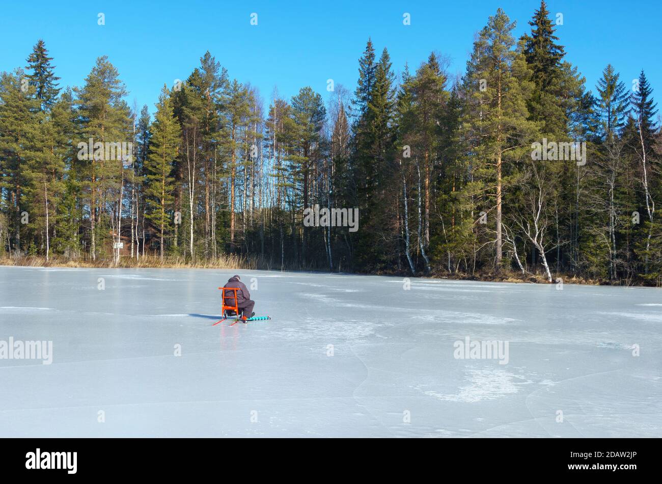 Homme âgé assis seul sur des kicksloed et la pêche sur glace sur le lac gelé à Winter, Finlande Banque D'Images