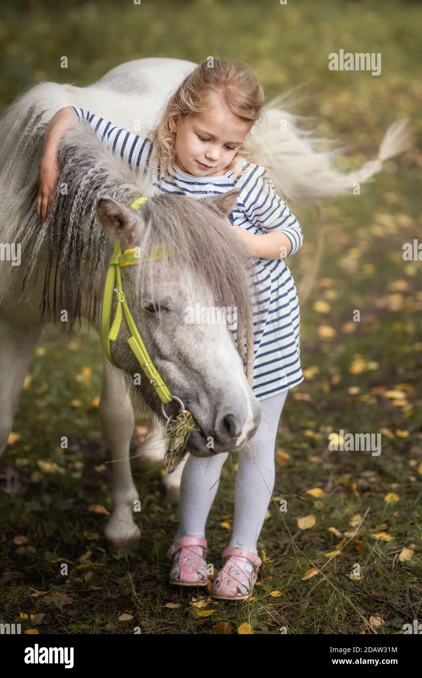 La petite fille blonde est debout près du poney du petit cheval et de l'embrasser Banque D'Images