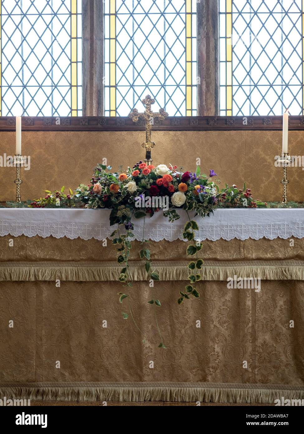 un arrangement de flore sur l'autel de l'église chrétienne sous le verre de tache fenêtre avec 2 bougies dans les supports équilibre symétrique en bas rétroéclairage lumineux Banque D'Images