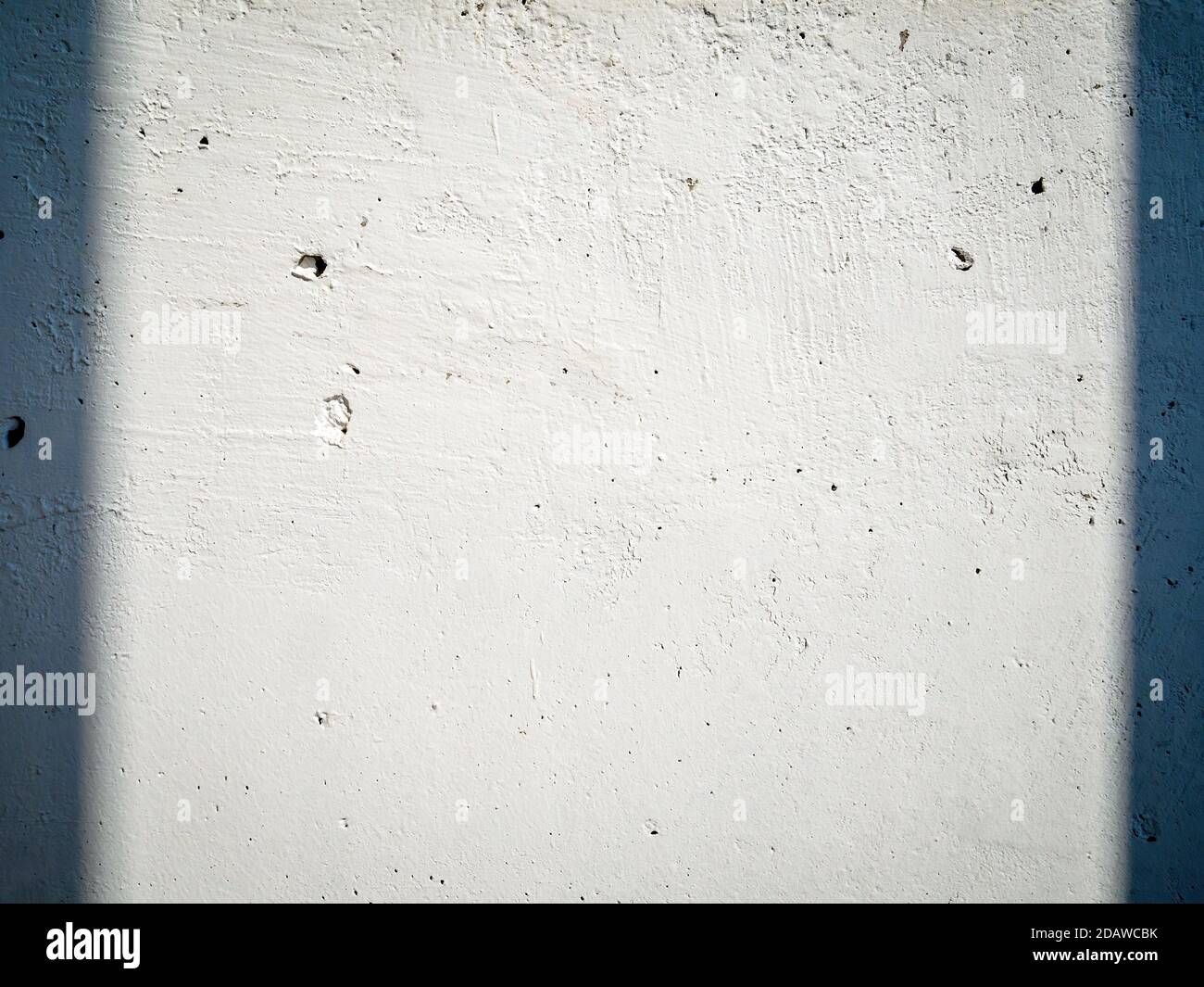 Le mur en béton blanc avec irrégularités est éclairé par le soleil et les ombres sur les côtés. Surface de bâtiment vide, espace de copie. Banque D'Images