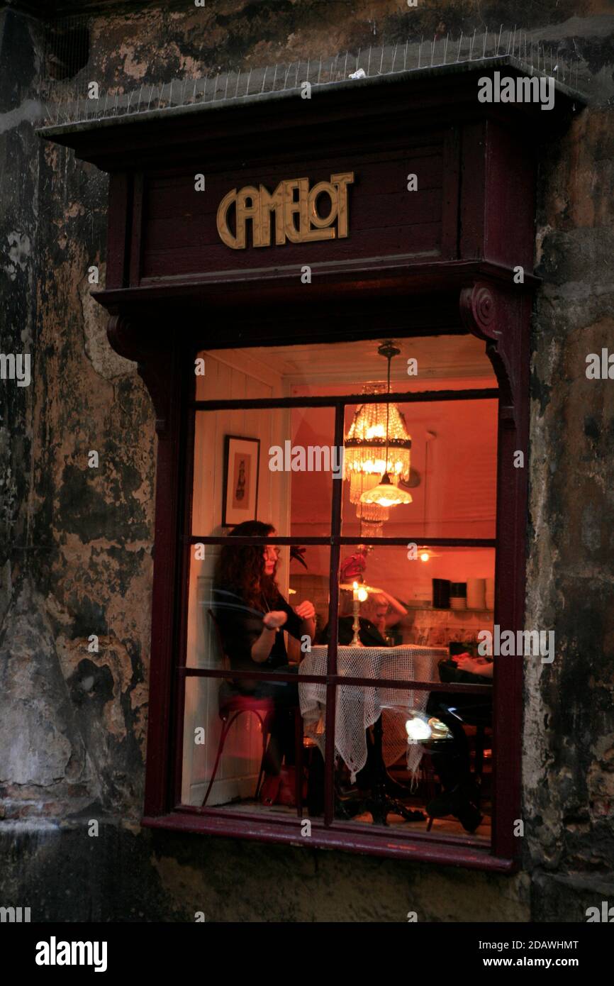 Une cliente dans une table lumineuse à fenêtre photographiée de l'extérieur au café Camelot, un café-restaurant renommé de Cracovie dans la vieille ville. Banque D'Images