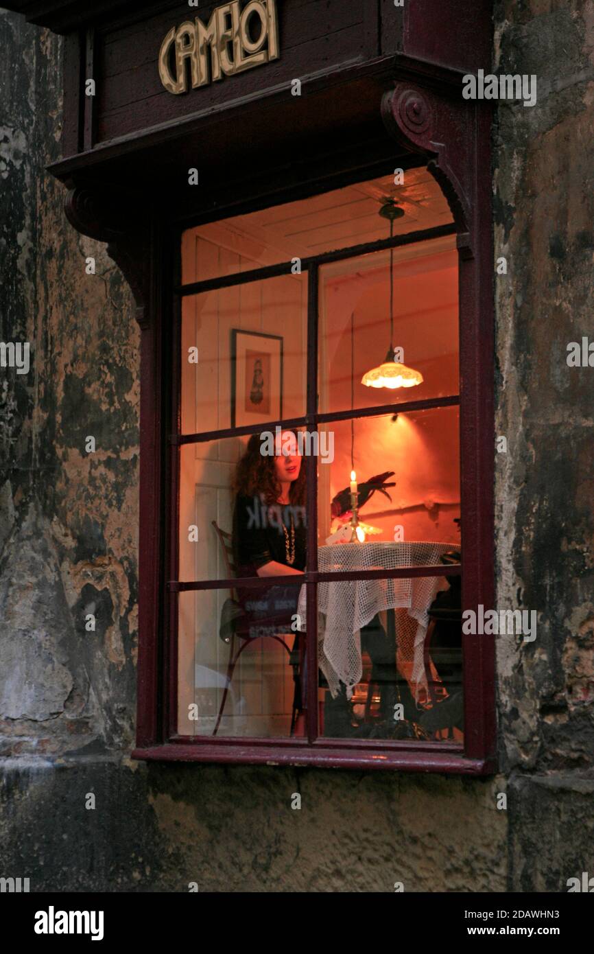 Une cliente dans une table lumineuse à fenêtre photographiée de l'extérieur au café Camelot, un café-restaurant renommé de Cracovie dans la vieille ville. Banque D'Images