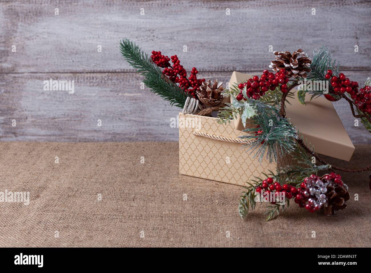 une carte en boîte cadeau beige et un Branche d'arbre de Noël avec des décorations sur un fond en bois et toile de jute Banque D'Images