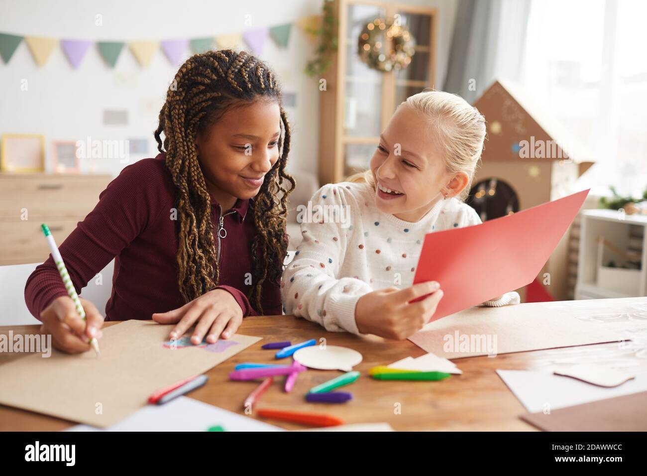 Portrait de deux filles adolescentes rieuses appréciant l'artisanat et la peinture faire un toether tout en vous assis sur le bureau dans la salle de jeux décorée Banque D'Images