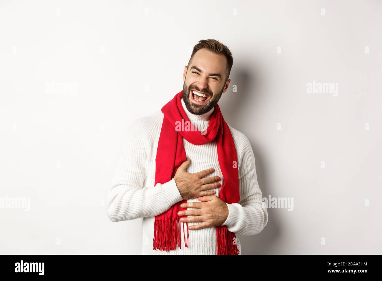 Un homme heureux riant et touchant le ventre, chatouillant d'une blague  drôle, debout dans un chandail d'hiver et une écharpe rouge, fond blanc  Photo Stock - Alamy