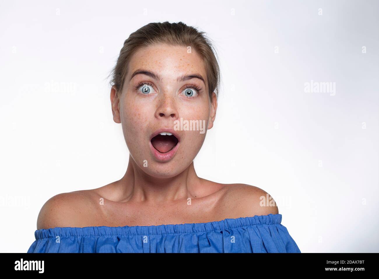 Belle fille avec des taches de rousseur montre des émotions devant le appareil photo sur fond blanc Banque D'Images