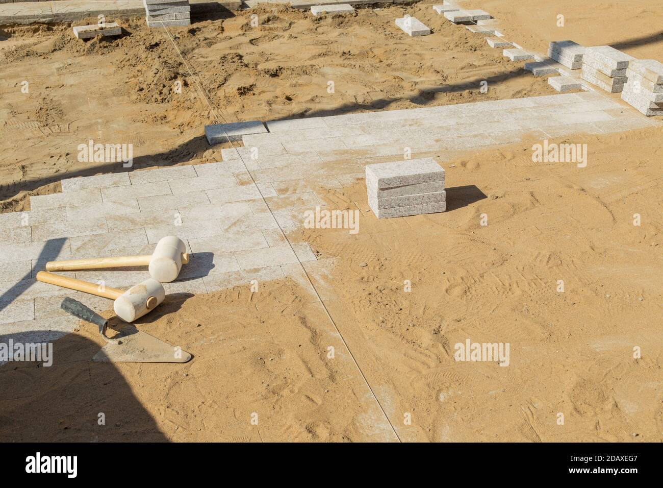 La truelle se trouve à côté de deux marteaux en caoutchouc pour poser des carreaux de sol sur des lingots de granit. Banque D'Images