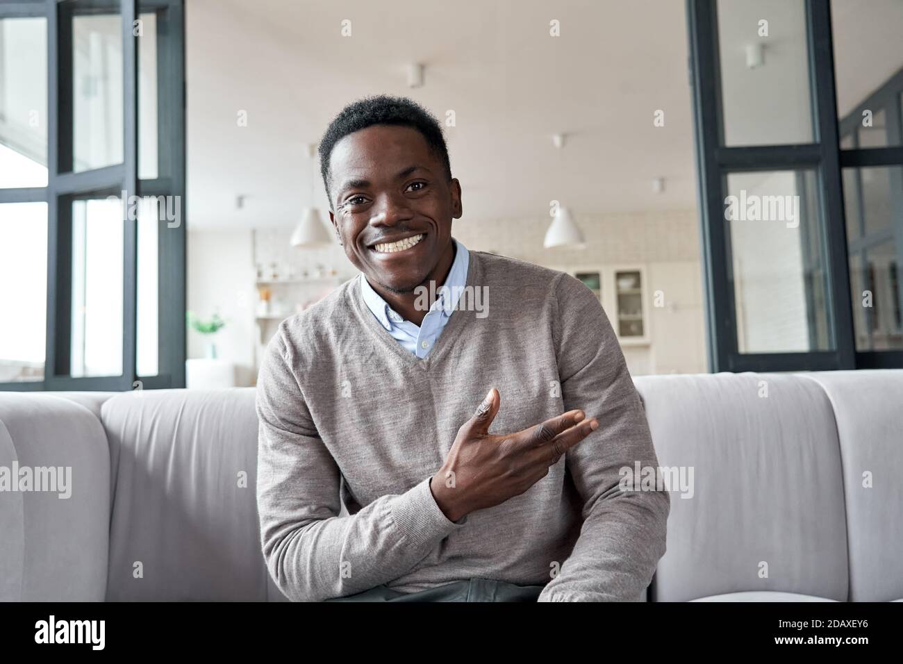 Joyeux jeune africain noir regardant la caméra assis sur le canapé à la maison. Banque D'Images