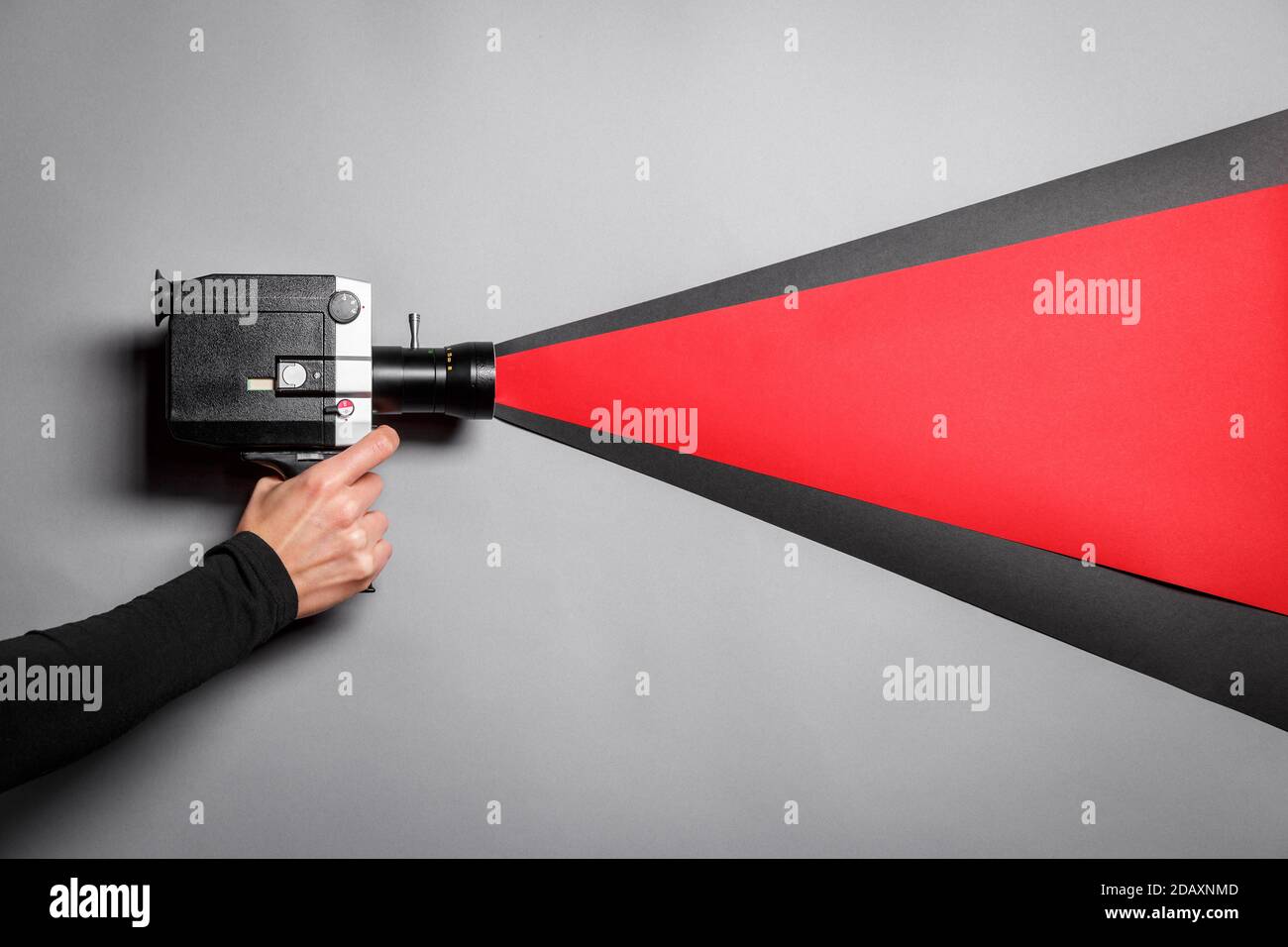 Main féminine tenant un ancien caméscope imitant le processus de prise de vue sur fond gris avec une lumière noire et rouge traversant l'objectif. Banque D'Images