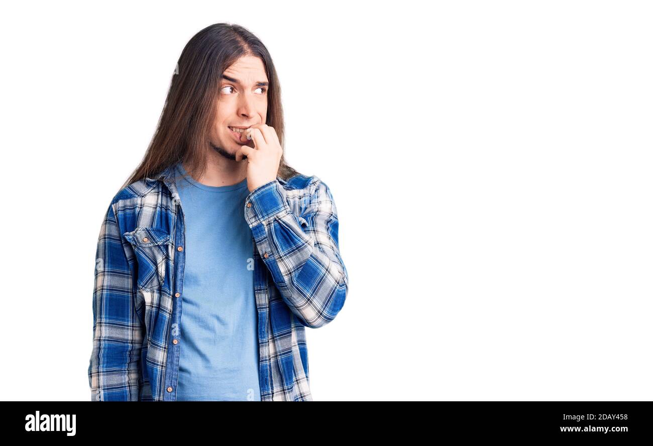 Jeune homme adulte avec de longs cheveux portant une chemise décontractée, aspect stressé et nerveux avec les mains sur la bouche mordant les ongles. Problème d'anxiété. Banque D'Images