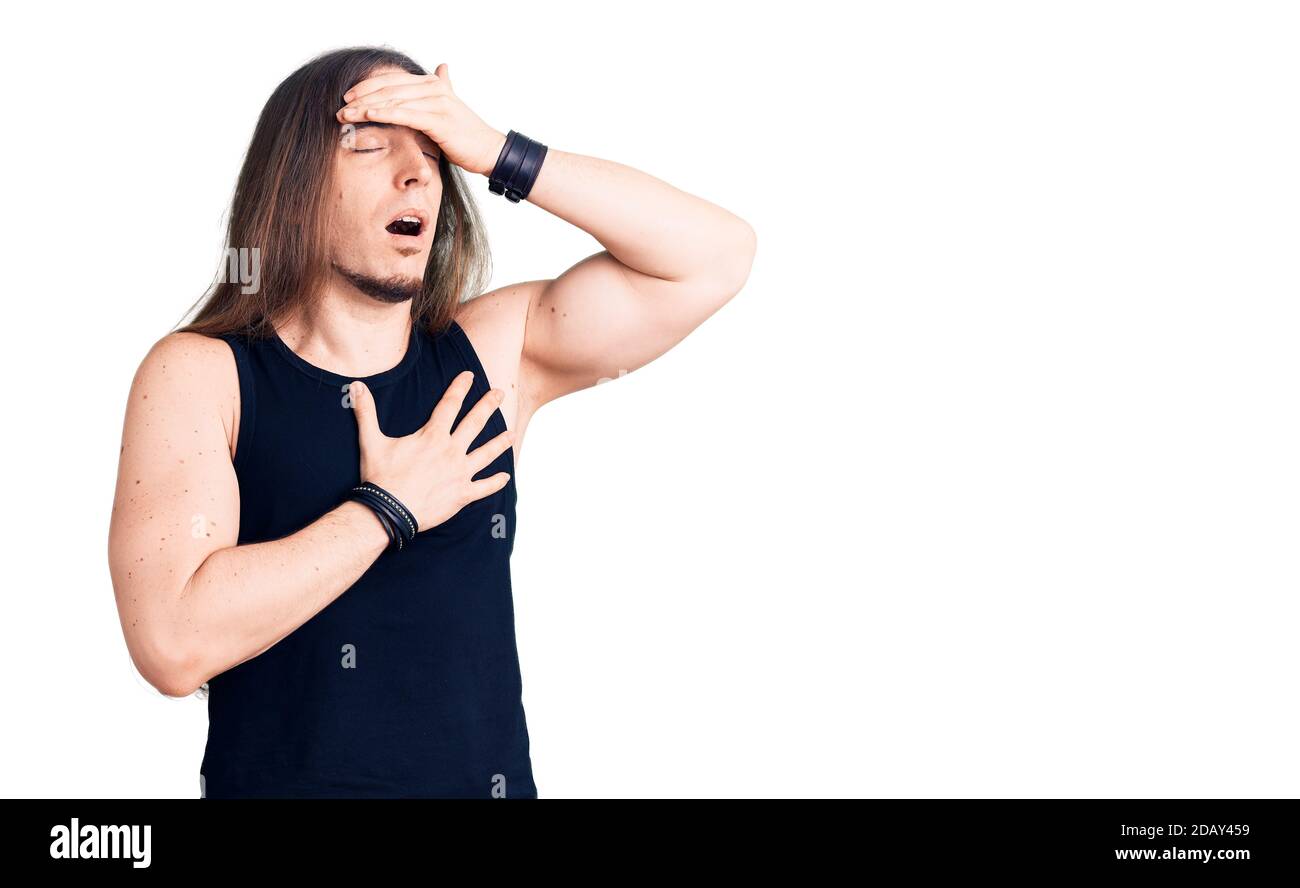 Jeune homme adulte avec de longs cheveux portant le style goth avec des vêtements noirs touchant le front pour la maladie et la fièvre, la grippe et le froid, virus malade Banque D'Images