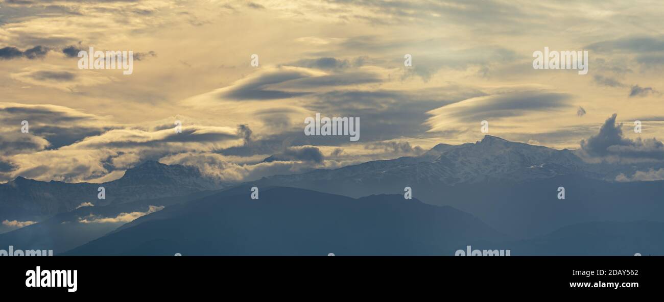 Vue panoramique sur la Sierra Nevada entre les nuages (certains d'entre eux lenticulaires) et des rayons de soleil au lever du soleil Banque D'Images