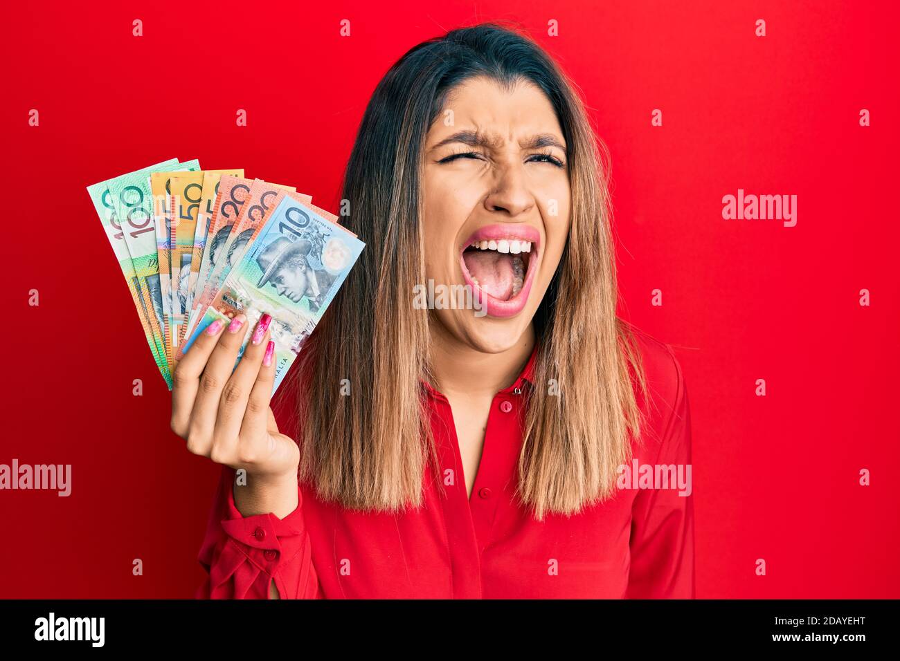 Belle femme brune tenant des dollars australiens en colère et folle hurlant frustré et furieux, criant avec colère. Rage et agressif concept. Banque D'Images