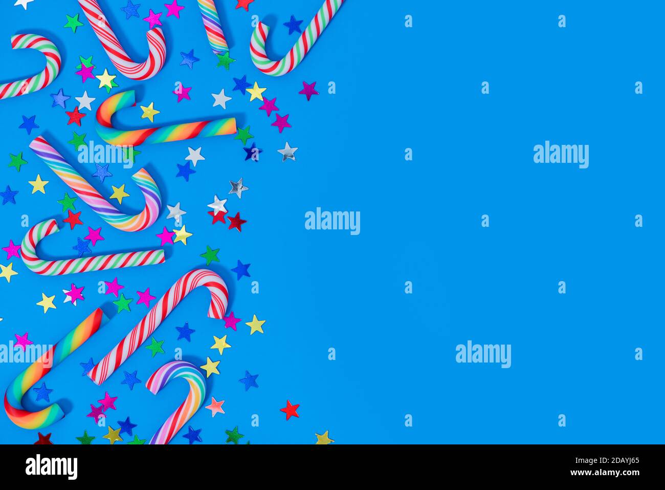 Fond de Noël avec différents confettis de canne à sucre et d'étoiles sur le bleu. Cannes en arc-en-ciel et glaçons traditionnels avec espace de copie. Banque D'Images