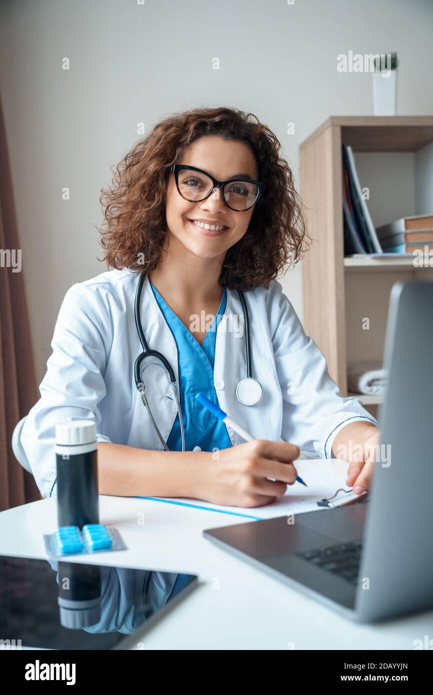 Portrait vertical d'une femme médecin assise sur le bureau et souriant à l'appareil photo. Banque D'Images