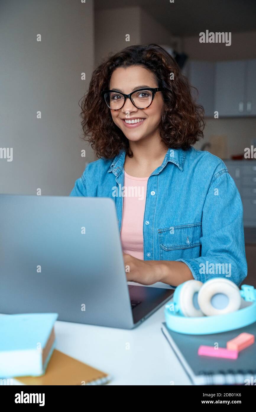 Bonne jeune étudiante latine étudiant en ligne sur ordinateur portable à la maison. Banque D'Images