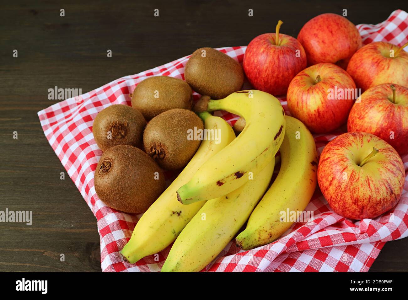 Tas de fruits kiwi mûrs frais, bananes et pommes sur un plateau avec un tissu à carreaux Banque D'Images