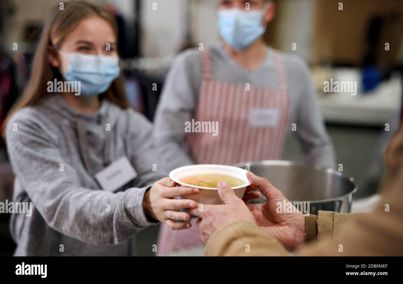 Bénévoles servant de la soupe chaude pour les sans-abri dans un centre de dons de charité communautaire, concept de coronavirus. Banque D'Images