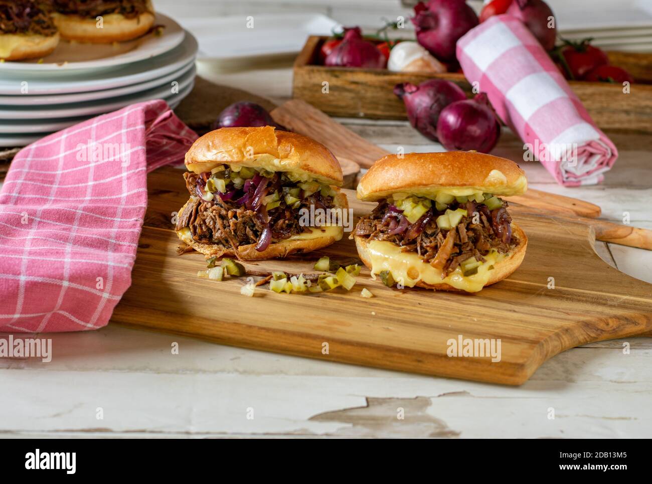 hamburger de bœuf tiré maison avec oignons rouges caramélisés, cornichons et fromage sur une planche de bois Banque D'Images