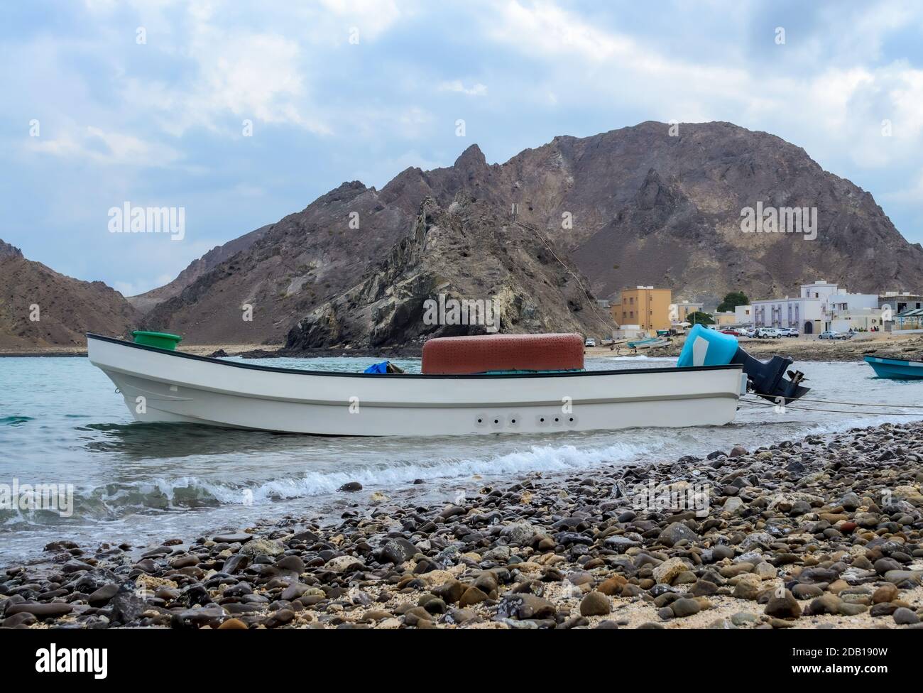 Petit bateau de pêche amarré sur la plage de Darsait, Muscat, Oman. Montagnes et village de pêcheurs en arrière-plan Banque D'Images