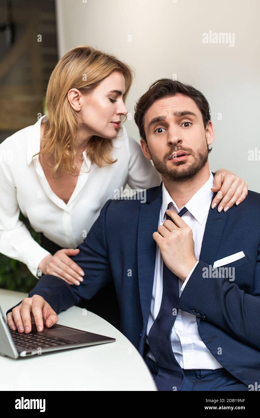 Séduction dans le concept de bureau. Jolie femme touchant un collègue masculin, qui s'assoit à la table, regardant la caméra brochée et touche sa cravate Banque D'Images