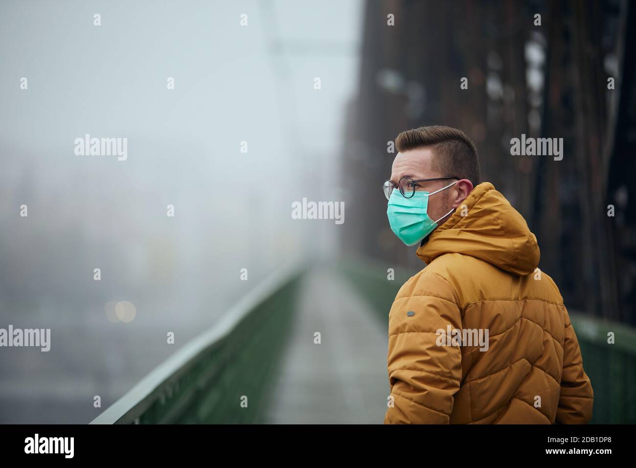 Solitaire avec masque de visage regardant en arrière pendant la marche sur le pont dans le brouillard. Thèmes la vie dans la nouvelle normale, coronavirus et la protection personnelle. Banque D'Images