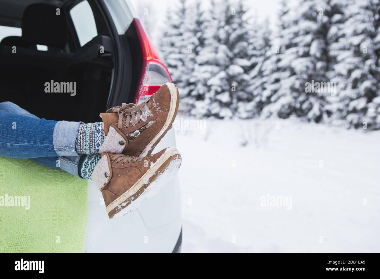 La femme est assise dans le coffre de la voiture. Gros plan des bottes d'hiver Banque D'Images