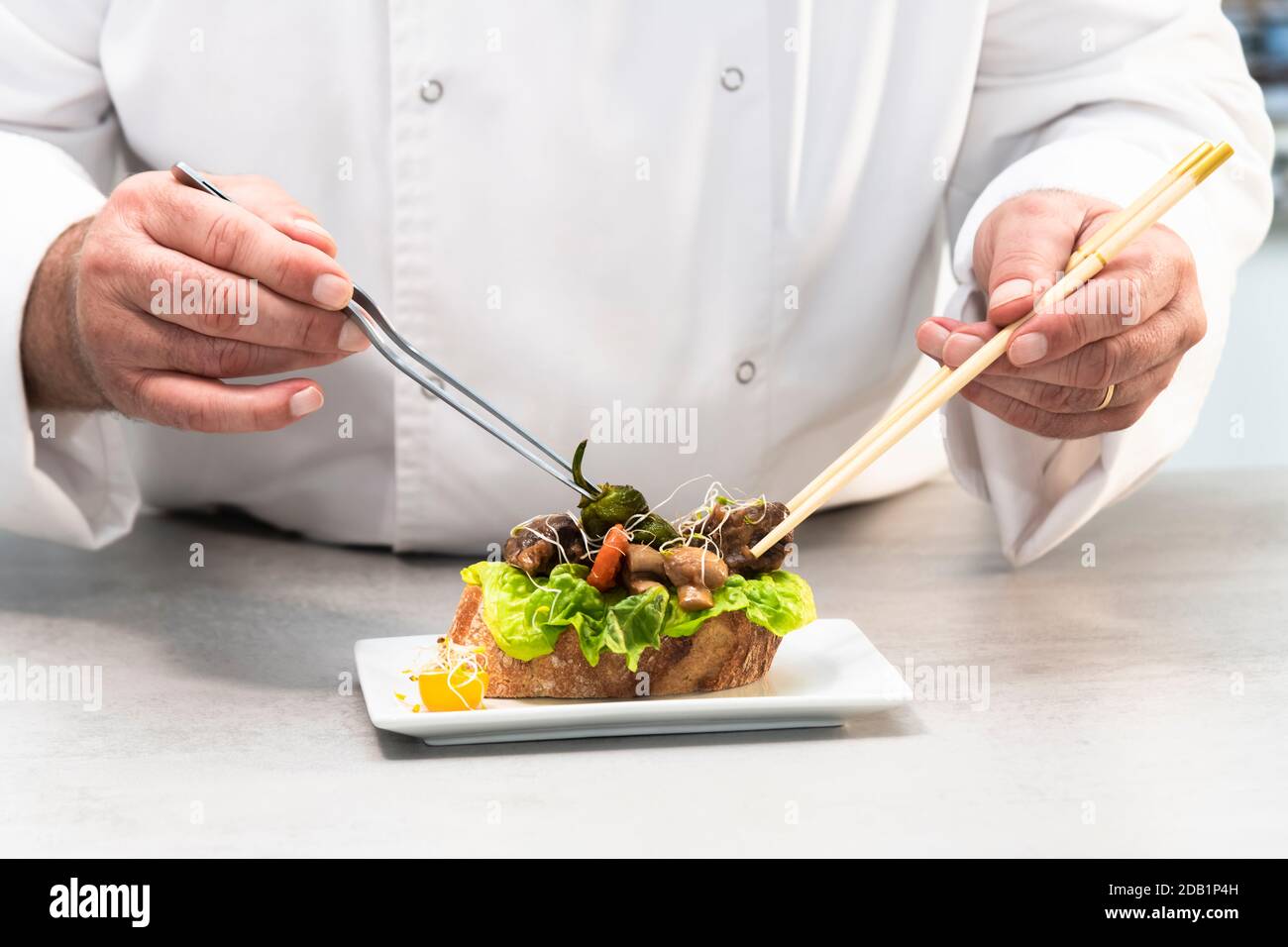 Objectif sélectif d'un chef masculin utilisant des pinces et des baguettes pour donner la touche finale à un appétissant sandwich ouvert. Concept d'alimentation saine. Banque D'Images