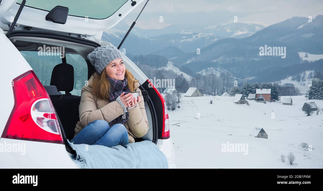 La femme est assise dans le coffre de la voiture et tient une tasse de thé chaud dans ses mains. Banque D'Images