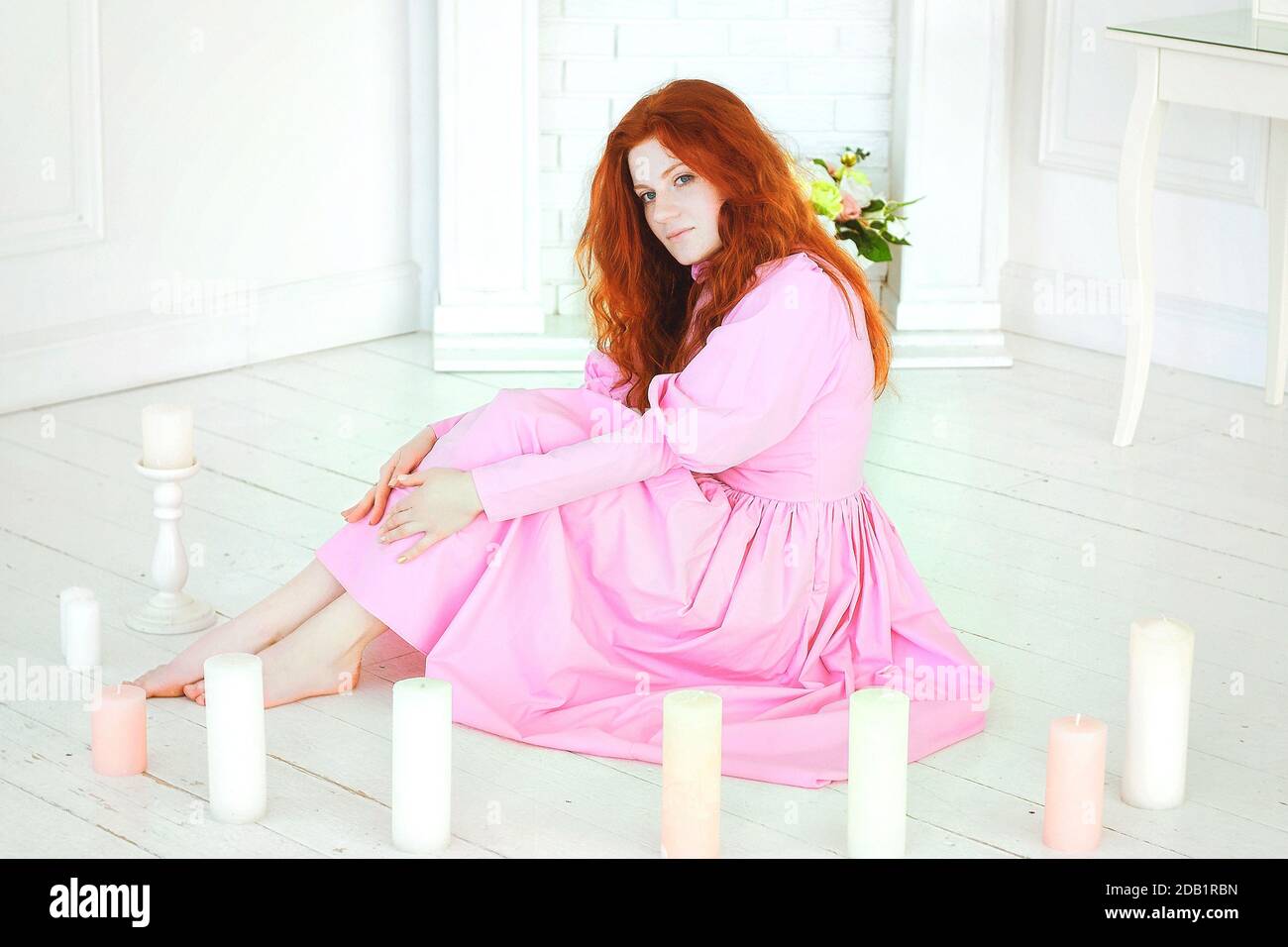 REDHEAD jolie femme dans une robe rose assis dans le soleil jour de printemps au studio et rêvant au sujet de la journée Womans. Banque D'Images