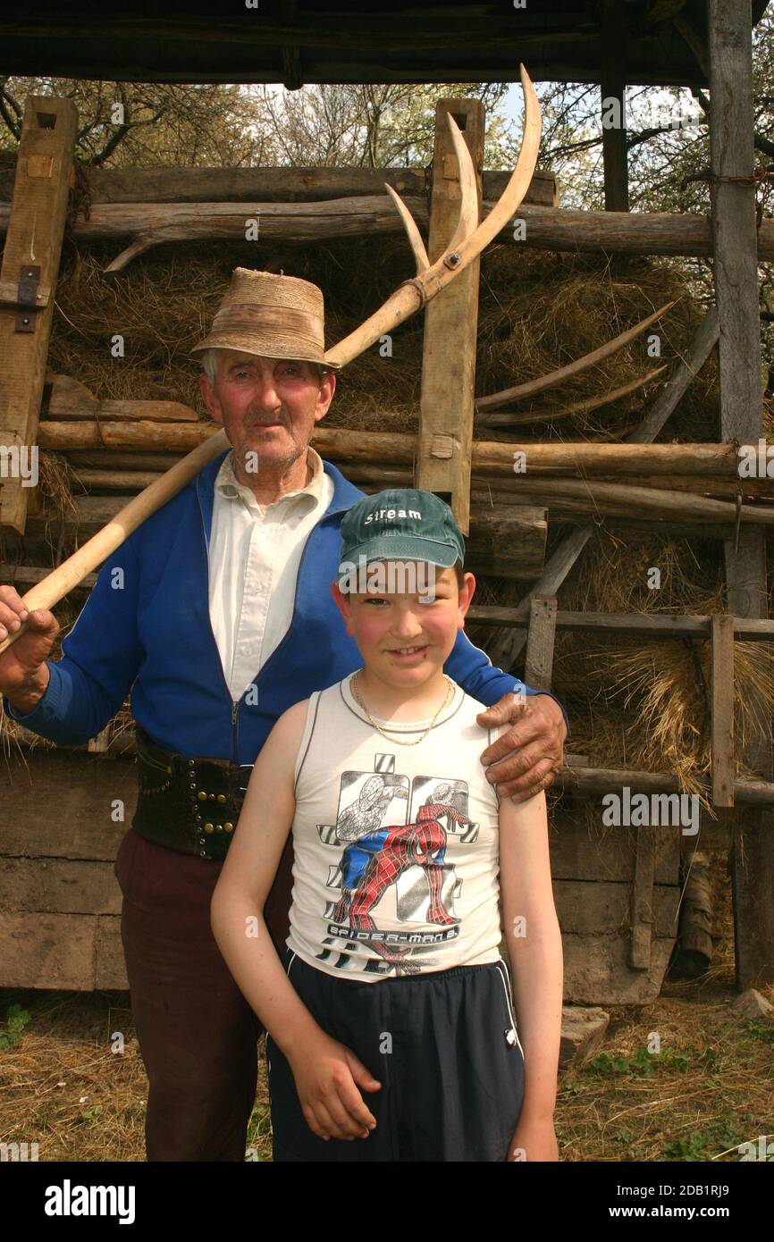 Maramures, Roumanie. Homme âgé avec une fourche en bois de foin posant avec son petit-enfant. Banque D'Images