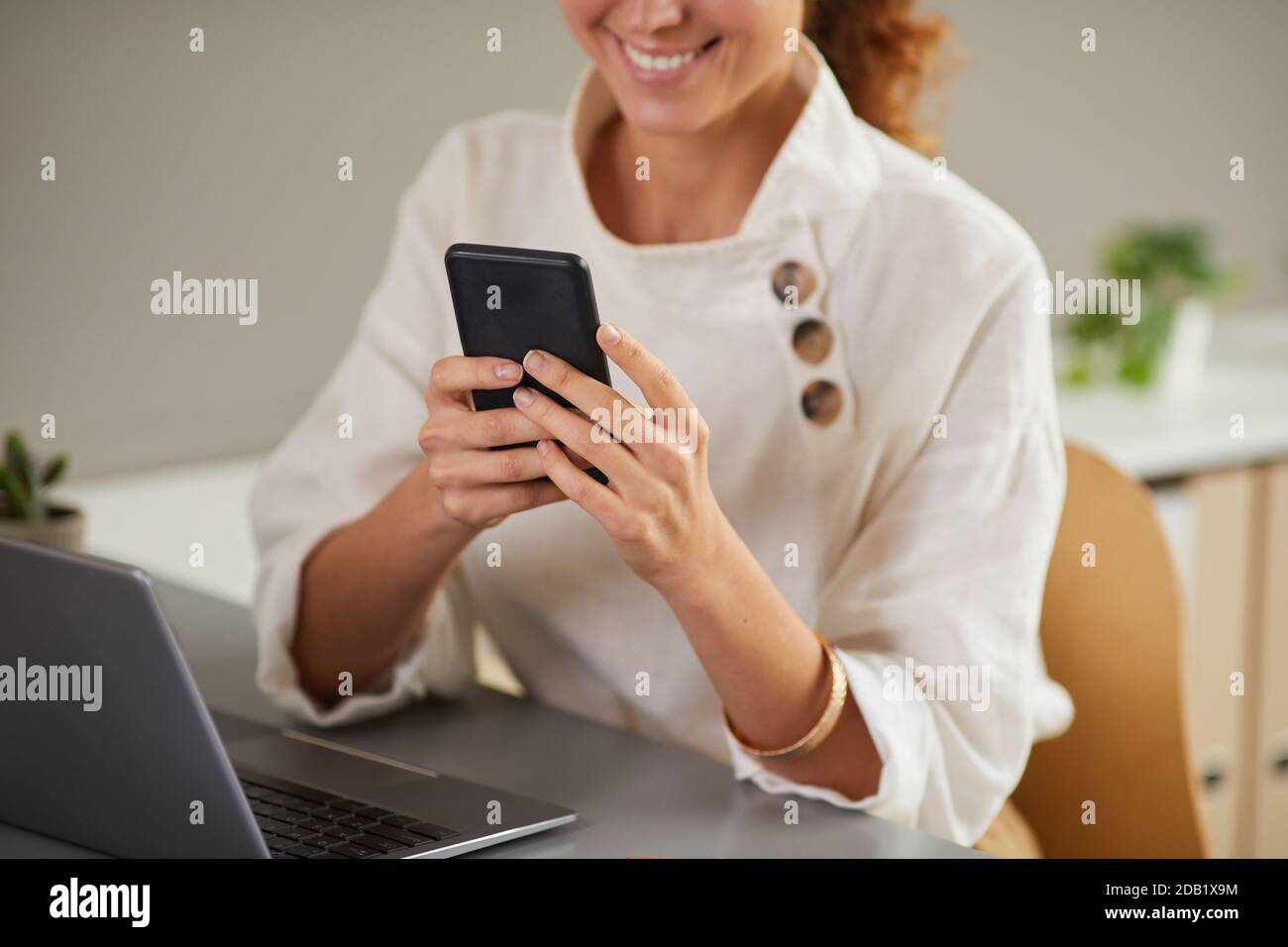Portrait rogné d'une jeune femme souriante utilisant un smartphone sur le lieu de travail tout en appréciant le travail à la maison, l'espace de copie Banque D'Images